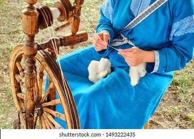 A woman in a blue dress spinning a spindle. Retro wooden wheel for thread making. - Powered by Shutterstock