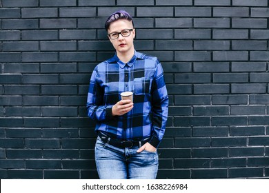 Woman In Blue Flannel Holding Paper Cup Against Black Wall