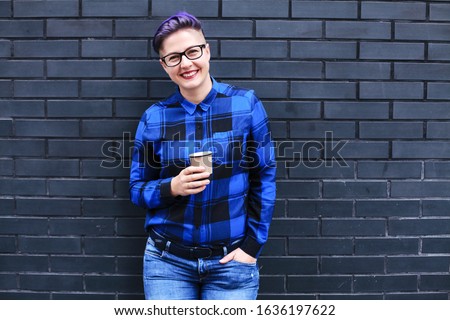 Woman in Blue Flannel Holding Paper Cup Against Black Wall