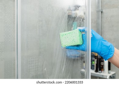 Woman in a blue glove cleans a shower cabin from limestone