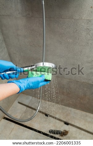Woman in a blue glove cleans a shower head from limestone. Close-up.