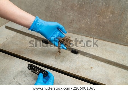 Woman in a blue glove removes hair clump from the shower drain.