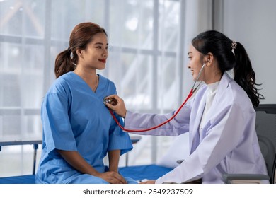 A woman in a blue hospital gown is being checked by a doctor. The doctor is using a stethoscope to listen to the woman's heart. Concept of care and concern for the patient's health - Powered by Shutterstock