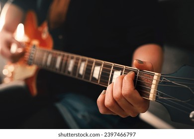 woman in blue hot pants plays chord on electric solidbody guitar with cherry sunburst body. selective focus on left hand with painted nails and first fret. colorful cinematic look