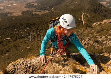 A woman in a blue jacket is climbing a mountain. She is wearing a helmet and a backpack