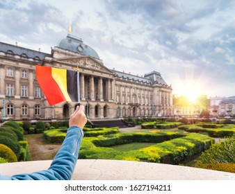 A woman in a blue jacket holds the flag of Belgium in the background of the Royal Palace in Brussels, Belgium