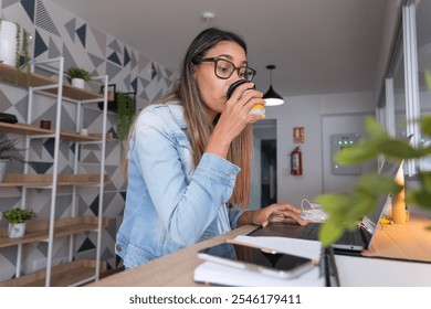 A woman in a blue jacket is sitting at a desk with a laptop and a cell phone. Coworking concept