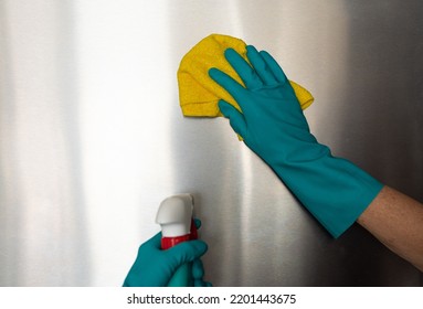 woman in blue rubber gloves dusts a switch with a microfibre cloth and uses a germ-removing spray. Cleaning concept, household introduction, clean house, no germs, covid-19