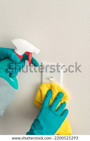 woman in blue rubber gloves dusts a switch with a microfibre cloth and uses a germ-removing spray. Cleaning concept, household introduction, clean house, no germs, covid-19 Foto stock © 
