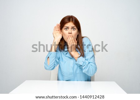 A woman in a blue shirt overhears a conversation and covers her mouth with her hand                       