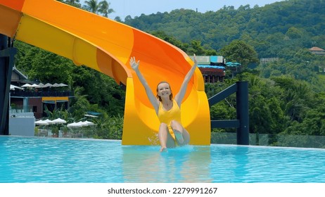 Woman in blue swimwear slides down a water slide at an aquapark resort, splashing into the pool. She enjoys the summer fun on vacation. Travel and holidays concept