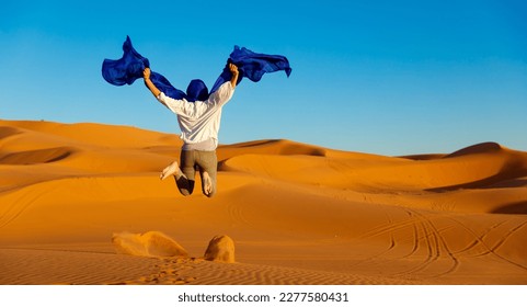 Woman with blue turban jumping in the desert- happiness,  travel,  freedom concept - Powered by Shutterstock