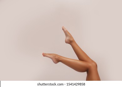 Woman body care. Close up of long female tanned legs with perfect smooth soft skin, pedicure, healthy nails on white background. Epilation, beauty and health concept
