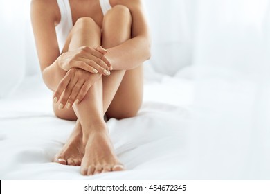 Woman Body Care. Close Up Of Long Female Legs With Perfect Smooth Soft Skin, Pedicure And Beautiful Hands With Natural Manicure, Healthy Nails On White Bed. Epilation, Beauty And Health Concepts