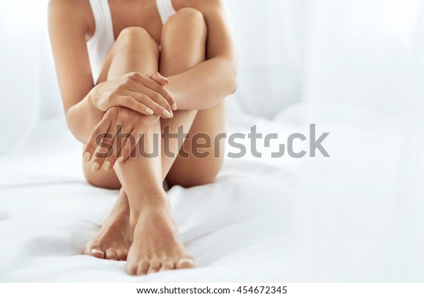 Woman Body Care. Close Up Of Long Female Legs\
With Perfect Smooth Soft Skin, Pedicure And Beautiful Hands With\
Natural Manicure, Healthy Nails On White Bed. Epilation, Beauty And\
Health Concepts