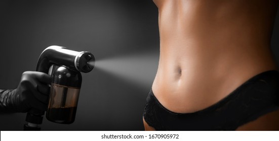 Woman body paint with airbrush spray tan in professional beauty salon on black background.