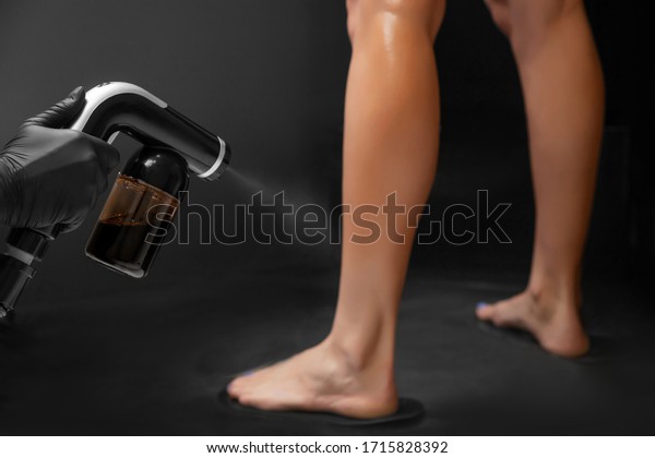 Woman body paint with airbrush spray
tan in professional beauty salon on black
background.