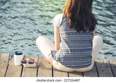 woman with a book, sunglasses and cup of coffee sitting on a pier - Powered by Shutterstock