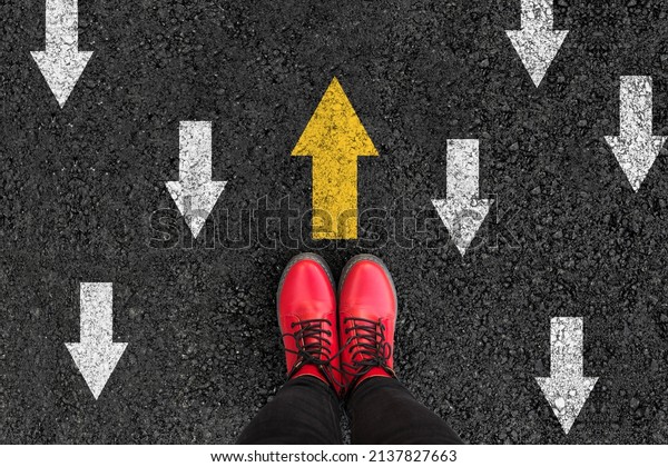 woman boots on asphalt and opposing direction arrows on\
asphalt ground, personal perspective footsie concept for finding\
your own way 