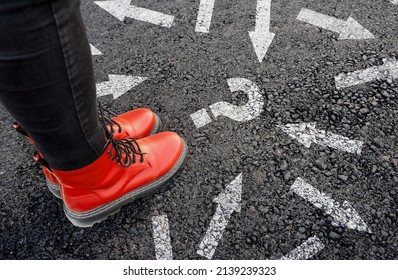 woman in boots standing on asphalt next to multitude of arrows in different directions and question mark, confusion choice chaos concept - Shutterstock ID 2139239323