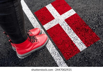 a woman with a boots standing on asphalt next to flag of Denmark and border 