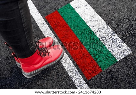 a woman with a boots standing on asphalt next to flag of Bulgaria and border 