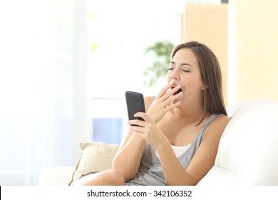 Woman Bored And Yawning Watching Media In A Mobile Phone Sitting On A Couch At Home