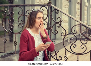 Woman Bored And Yawning Watching Media In A Mobile Phone Sitting Outdoors Outside Near Her Home In Manhattan New York