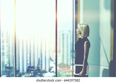 Woman Boss With Digital Tablet In Hand Is Watching In Office Window With Copy Space For Content, While Is Resting After Conference With Her Staff. Female Manager Is Thinking About Future Work Plan