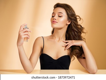 Woman with bottle of perfume. Photo of woman with perfect makeup on beige background. Beauty concept