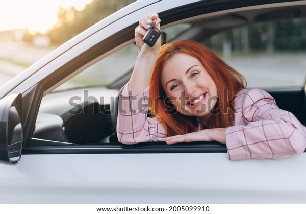 Woman bought first car. Joyful female sitting in\
new car and shows keys.