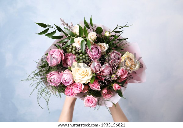 Woman with bouquet of beautiful roses on light\
blue background, closeup