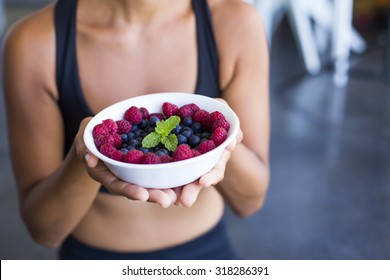 Woman with a bowl of berries wearing a sportive outfit.