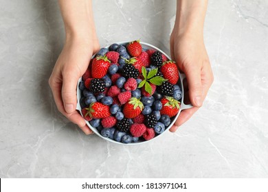 Woman with bowl of delicious berries at light table, closeup - Powered by Shutterstock