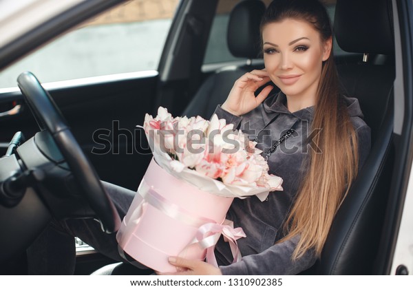 woman with box of flowers sitting in\
car.   happy girl with flower bouquet for\
holiday