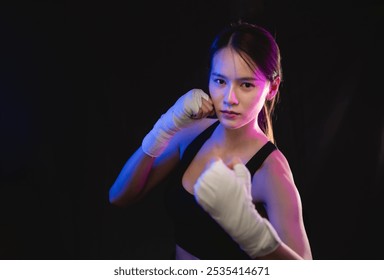 A woman is boxing in a dark room. She is wearing gloves and a black top. She is in the middle of a punch - Powered by Shutterstock