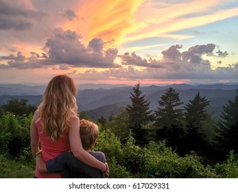 A woman and a boy look at a sunset over a mountain range in the Blue Ridge Mountains on the Blue Ridge Parkway in Western North Carolina