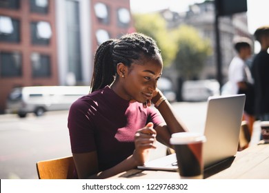 Woman With Braids Using A Laptop At An Outdoor Cafe