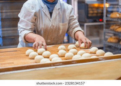 Woman breadmaker employee in the artisan bakery workshop preparing the dough in a circle - Powered by Shutterstock