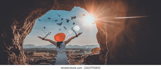 The woman is breaking the chains and setting the birds free, in a cave at the top of a mountain enjoying the nature at sunrise. concept of freedom