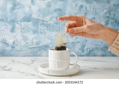 Woman Brewing Tea With Bag In Cup On Color Background