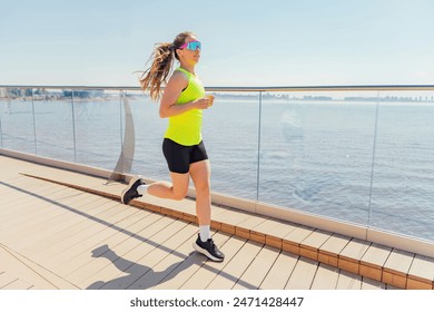 Woman in a bright yellow tank top jogs along a waterfront boardwalk on a sunny day. - Powered by Shutterstock