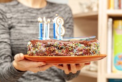 A Woman Bringing In A Delicious Homemade Birthday Cake, Brown Cocoa Chocolate Cake With Sprinkles, Icing And Candles, Holding A Plate. Childs Birthday, Sweet Food, Closeup. Birthday Cake On A Plate
