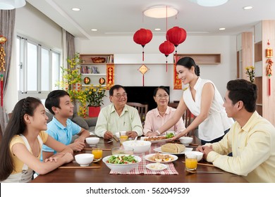 Woman bringing main dish to dinner table for Tet celebration; couplets with best wishes for coming year in the background