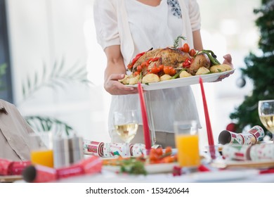 Woman Bringing Roast Chicken At Table For Christmas Dinner