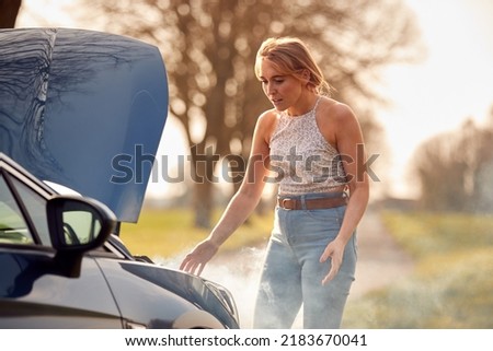 Woman Broken Down On Country Road Looking Under Smoking Bonnet Of Car
