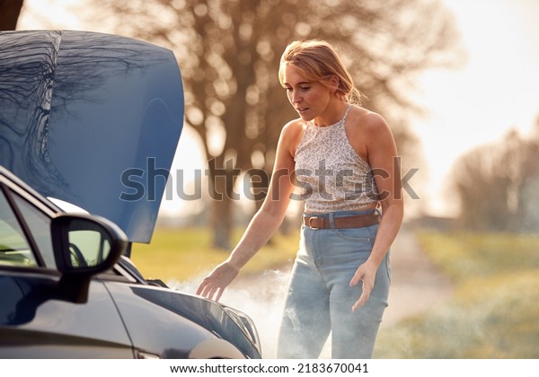 Woman Broken Down On Country Road Looking Under\
Smoking Bonnet Of Car