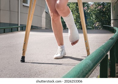 Eine Frau mit gebrochenem Bein geht mit orthopädischen Krücken über eine Ra...