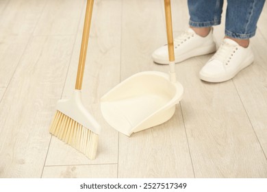 Woman with broom and dustpan cleaning floor indoors, closeup - Powered by Shutterstock