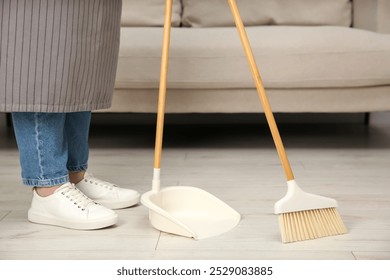 Woman with broom and dustpan cleaning floor indoors, closeup - Powered by Shutterstock